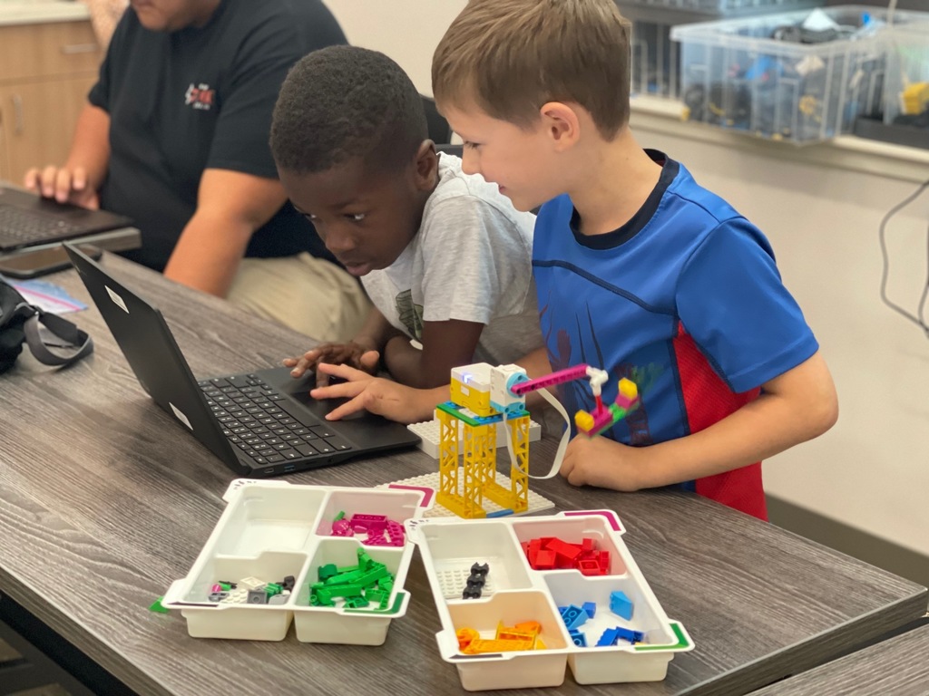Two boys looking at computer with legos on the table.